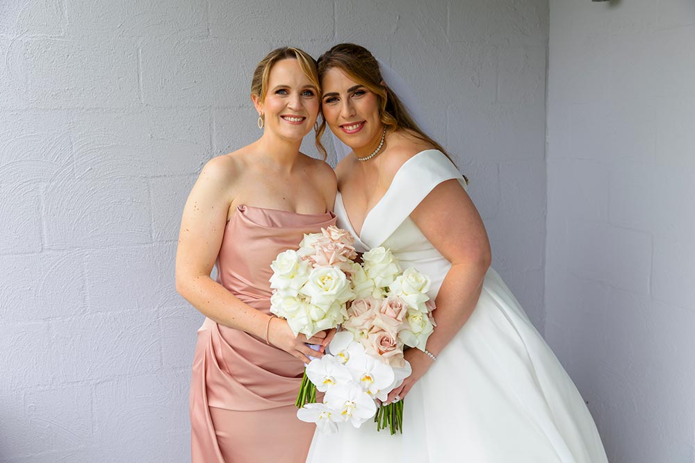 bride with bridesmaid in pink dress with white roses